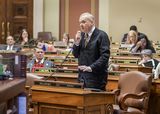 Representative Pelowski stands at his desk in the House Chamber and speaks into a microphone to someone out of view.